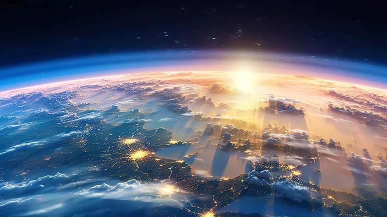 Sunrise over Earth from space, illuminating factory lights below.