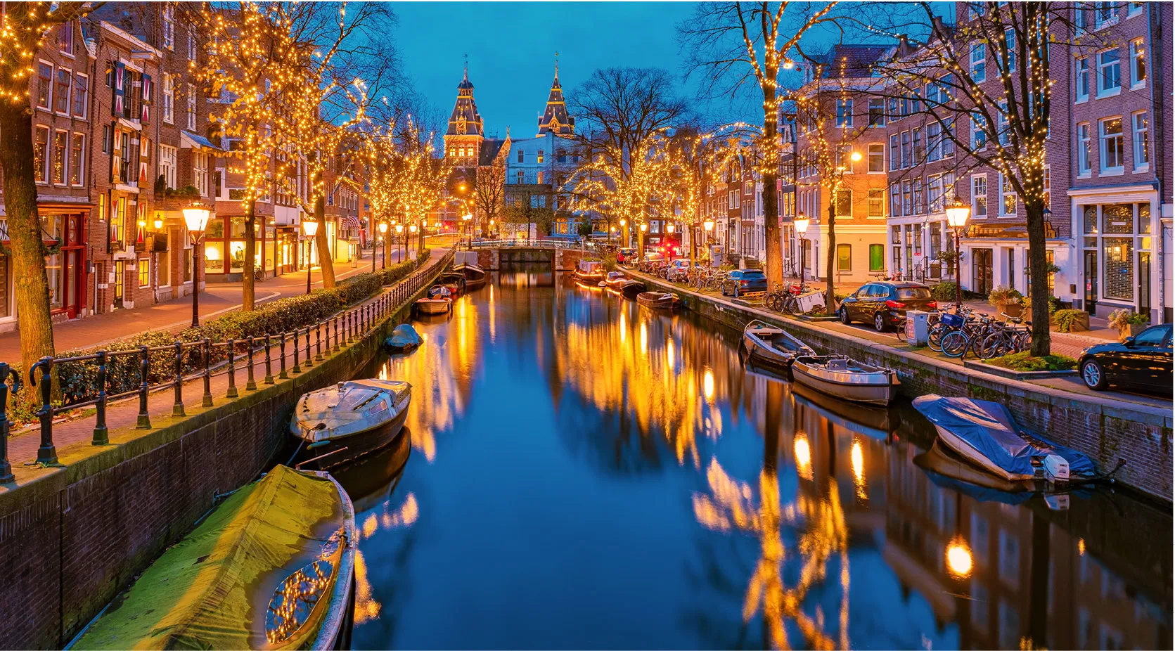 Amsterdam canal at night with illuminated trees, boats, and buildings.