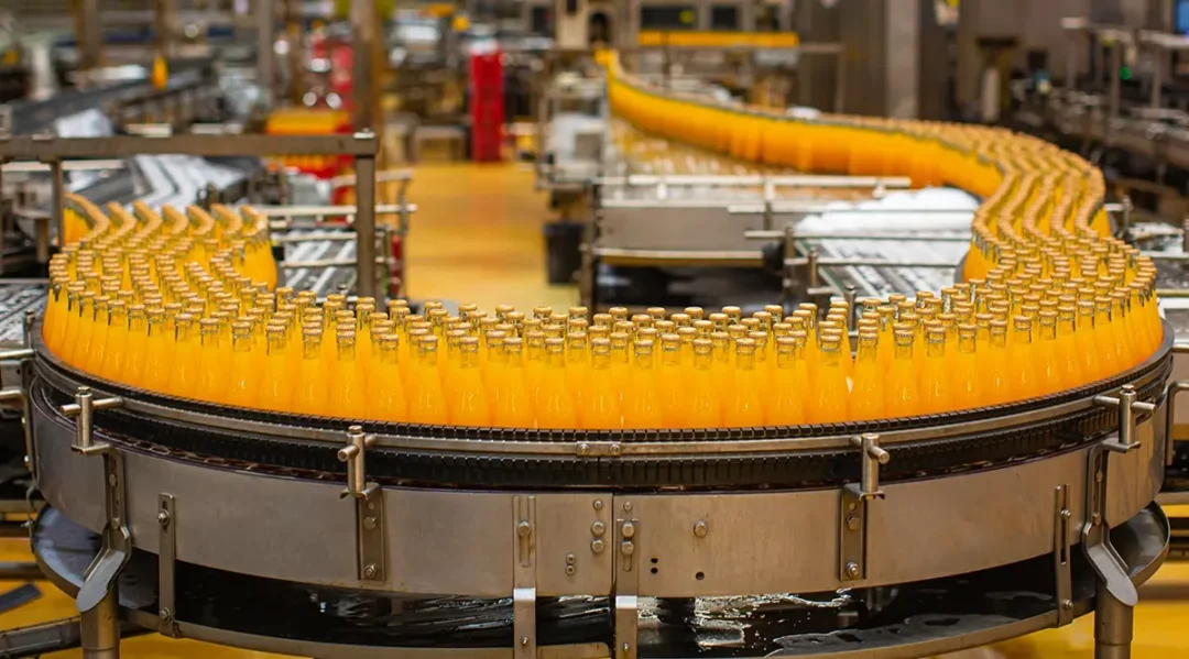 Bottles of orange juice on a conveyor belt in a beverage factory, illustrating supply chain automation.